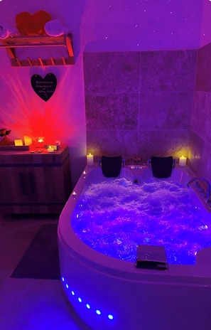 A spa room with a hot tub, candles, and a heart-shaped decoration on the wall. - Cocon Love Spa balnéo 32 jets, Lit Rond XXL, Douche ciel de pluie Aigues-Mortes (Aigues-Mortes)
