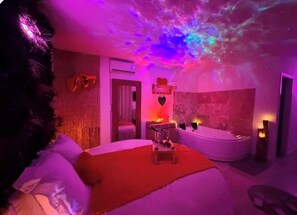 A room with a bed, a small table, a bathtub, and a wall with a celestial projection. - Cocon Love Spa balnéo 32 jets, Lit Rond XXL, Douche ciel de pluie Aigues-Mortes (Aigues-Mortes)