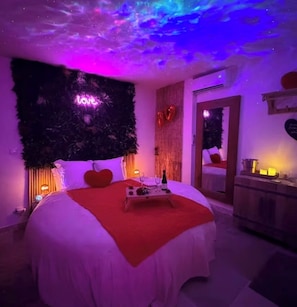 A bedroom with a bed, a nightstand, a dresser, and a wall-mounted TV. - Cocon Love Spa balnéo 32 jets, Lit Rond XXL, Douche ciel de pluie Aigues-Mortes (Aigues-Mortes)