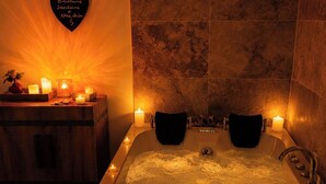Spa-huone, jossa on suuri kylpyamme, kynttilöitä ja sydämenmuotoinen koriste seinällä.