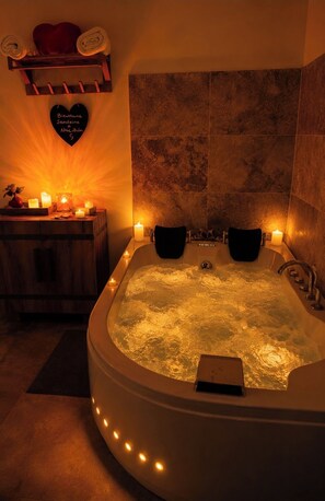 A spa room with a large bathtub, candles, and a heart-shaped sign on the wall. - Cocon Love Spa balnéo 32 jets, Lit Rond XXL, Douche ciel de pluie Aigues-Mortes (Aigues-Mortes)