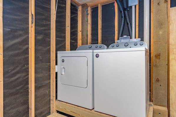 A compact, single-washer unit with a front door and control knobs, installed in a wooden-framed space with insulation visible on the walls. - The Canady Cottage- 3 BR Home Located on a Quiet Street (Topsail Beach)