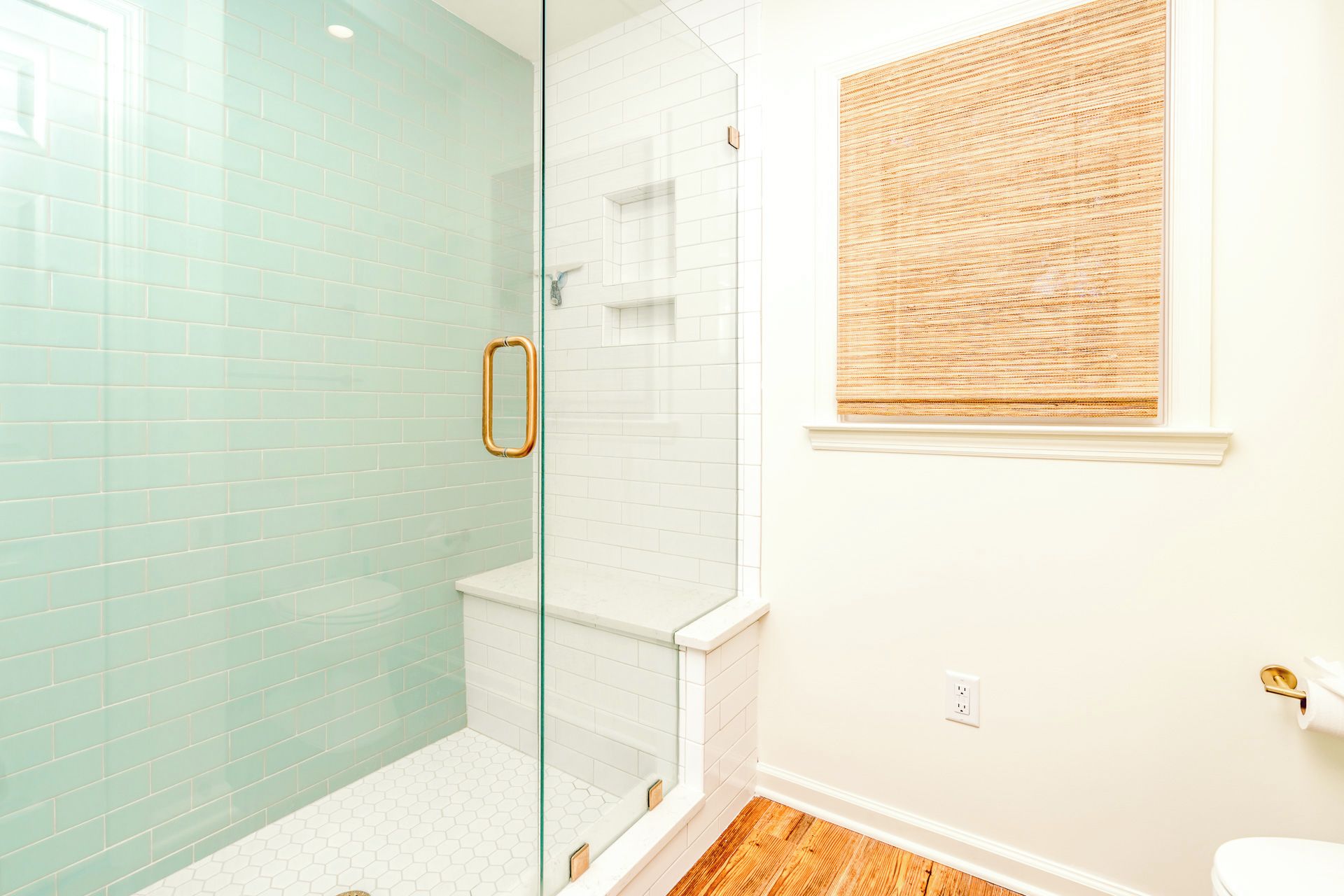 A bathroom with a glass shower enclosure, a toilet, and a window with a bamboo blind.