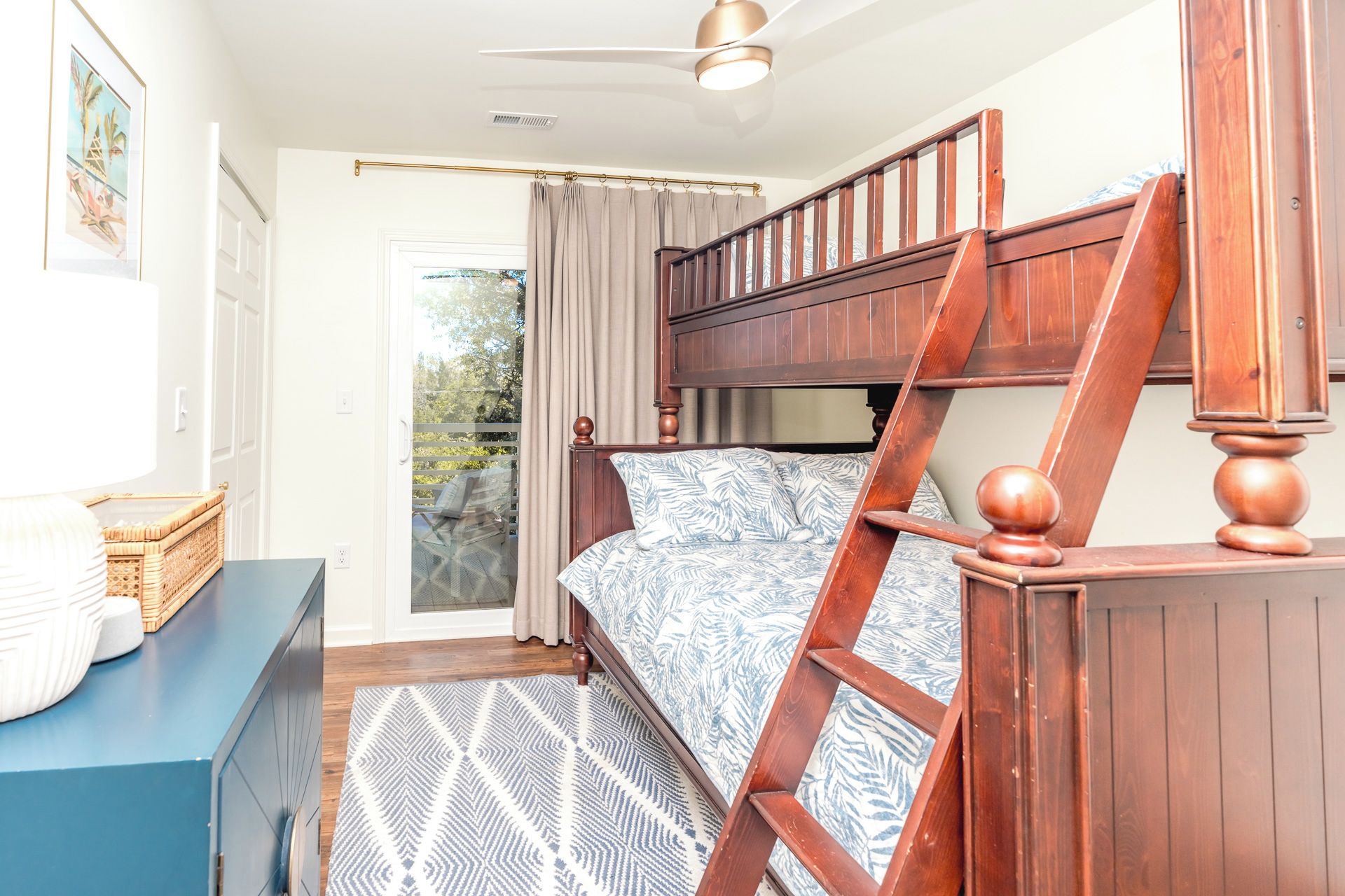 Een slaapkamer met een houten stapelbed, een plafondventilator, een raam met gordijnen en uitzicht op de omgeving.