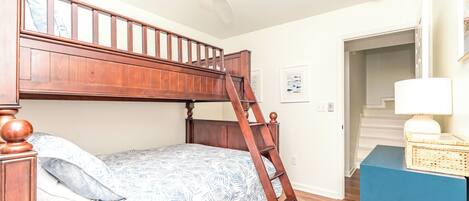 A bunk bed with a wooden ladder, a patterned bedspread, a blue bedside table, and a white wall with a framed picture.