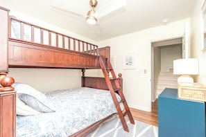A bunk bed with a wooden ladder, a patterned bedspread, a blue bedside table, and a white wall with a framed picture. - The Canady Cottage- 3 BR Home Located on a Quiet Street (Topsail Beach)