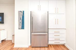 A kitchen with a stainless steel refrigerator, white cabinets, and a wooden floor. - The Canady Cottage- 3 BR Home Located on a Quiet Street (Topsail Beach)