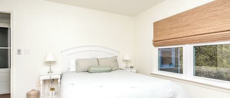 A bedroom with a bed, bedside tables, a ceiling fan, a window with a view, and a door.