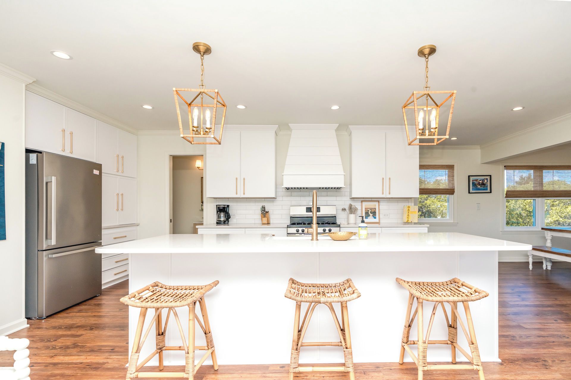 Una cocina moderna con armarios blancos, una isla central con taburetes, un refrigerador de acero inoxidable e iluminación colgante.