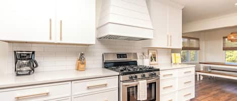 A modern kitchen with white cabinetry, a gas stove, and a coffee maker.