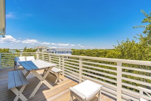 A wooden deck with white railings, outdoor seating, and a view of houses and greenery. - The Canady Cottage- 3 BR Home Located on a Quiet Street (Topsail Beach)