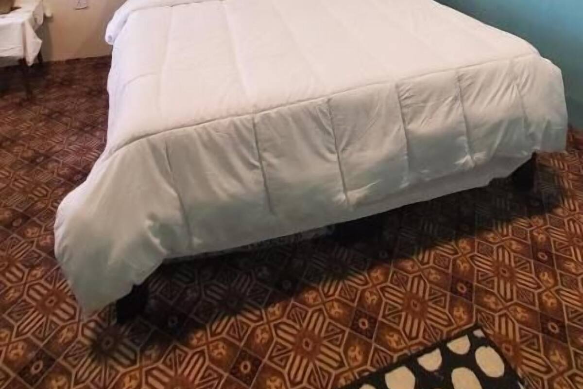 A bedroom with a bed, a ceiling fan, patterned floor tiles, and a nightstand.