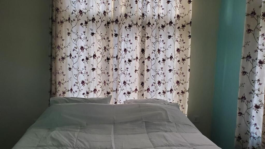 Una habitación con cama, cortinas florales y una pared color turquesa.