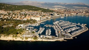 En vy över en kuststad från ovan, med en småbåtshamn, byggnader och berg i bakgrunden.