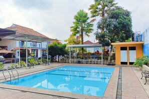 A swimming pool with a tiled deck, surrounded by buildings and trees. - TwoSpaces Living at Matahari Homestay (Batu)