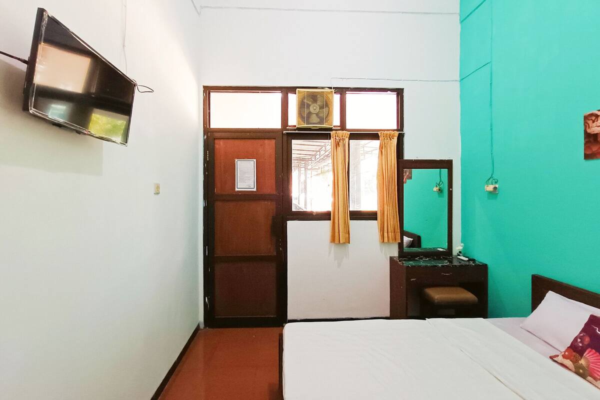 A room with a bed, a TV mounted on the wall, a window with curtains, and a green wall.