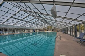 Una piscina techada con paneles de vidrio, sillas de descanso y vistas despejadas al exterior.