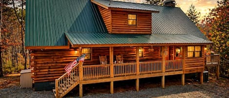 A log cabin with a porch, a small upper deck, and a flag.