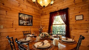 A wooden cabin dining room with a round table set for four, a chandelier, and a painting on the wall. - Rustic Cabin Getaway with Cozy Charm & Serene Surroundings in Gilmer County, Georgia (Gilmer County)