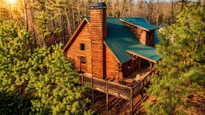 A log cabin with a green roof, a porch with chairs, and a chimney. - Rustic Cabin Getaway with Cozy Charm & Serene Surroundings in Gilmer County, Georgia (Gilmer County)