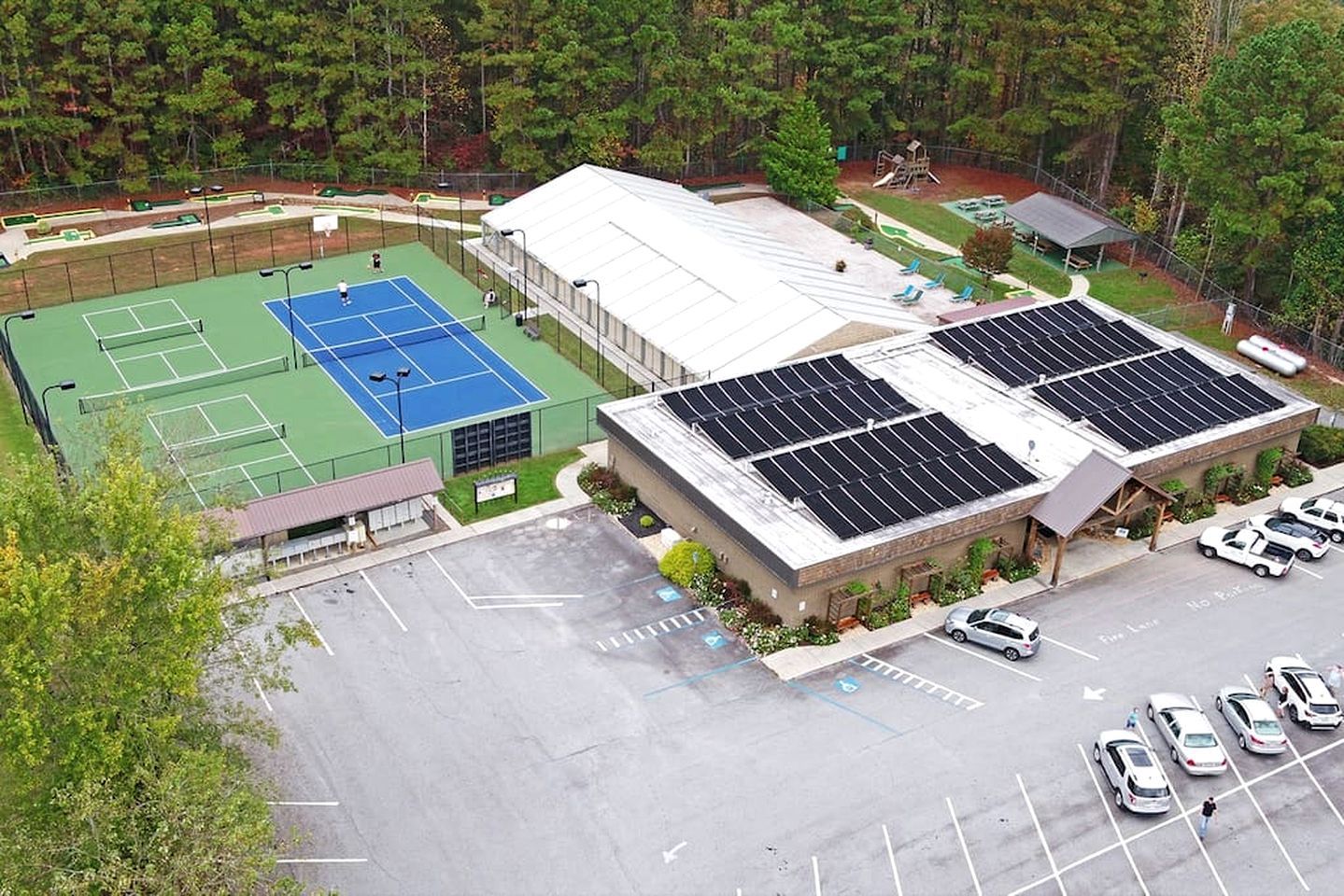 A building with solar panels, a tennis court, and a parking lot.