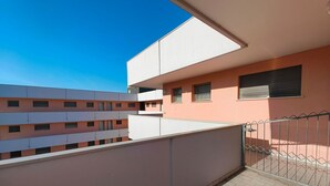Een meerhoog gebouw met balkons, een metalen hek en een helderblauwe lucht.