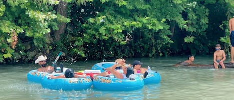 Personas flotando en botes inflables azules en un río rodeado de árboles.