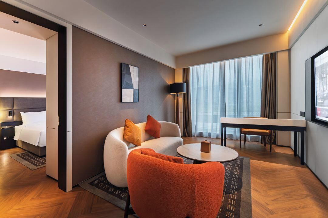 A hotel room with a bed, a sofa, a dining table, and a TV.
