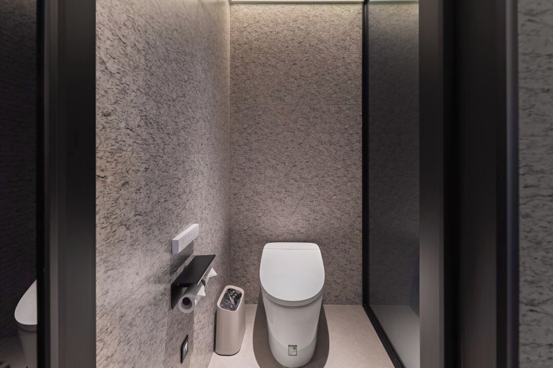 A modern bathroom with a marble wall, a toilet, a trash bin, and a hand dryer.