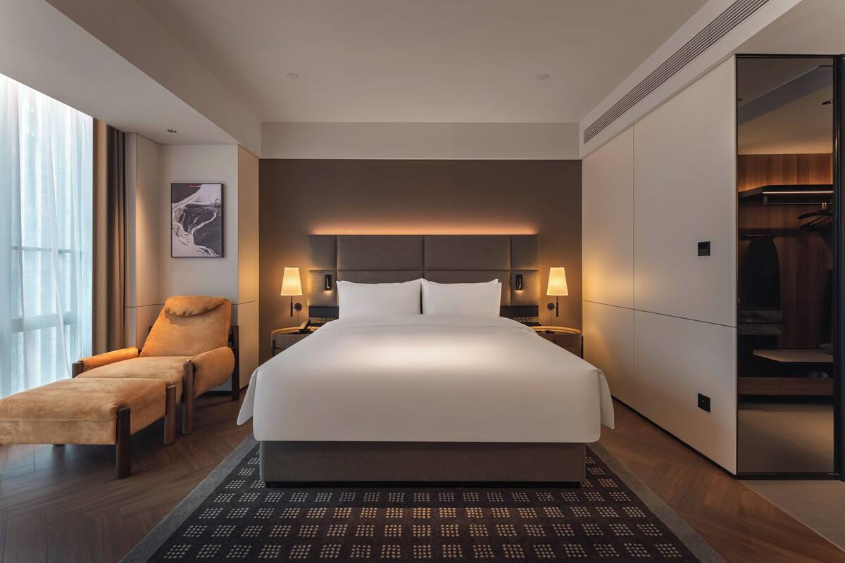 Ein modernes Hotelzimmer mit einem großen Bett, einer Sitzecke, einem Kleiderschrank und Blick ins Freie.
