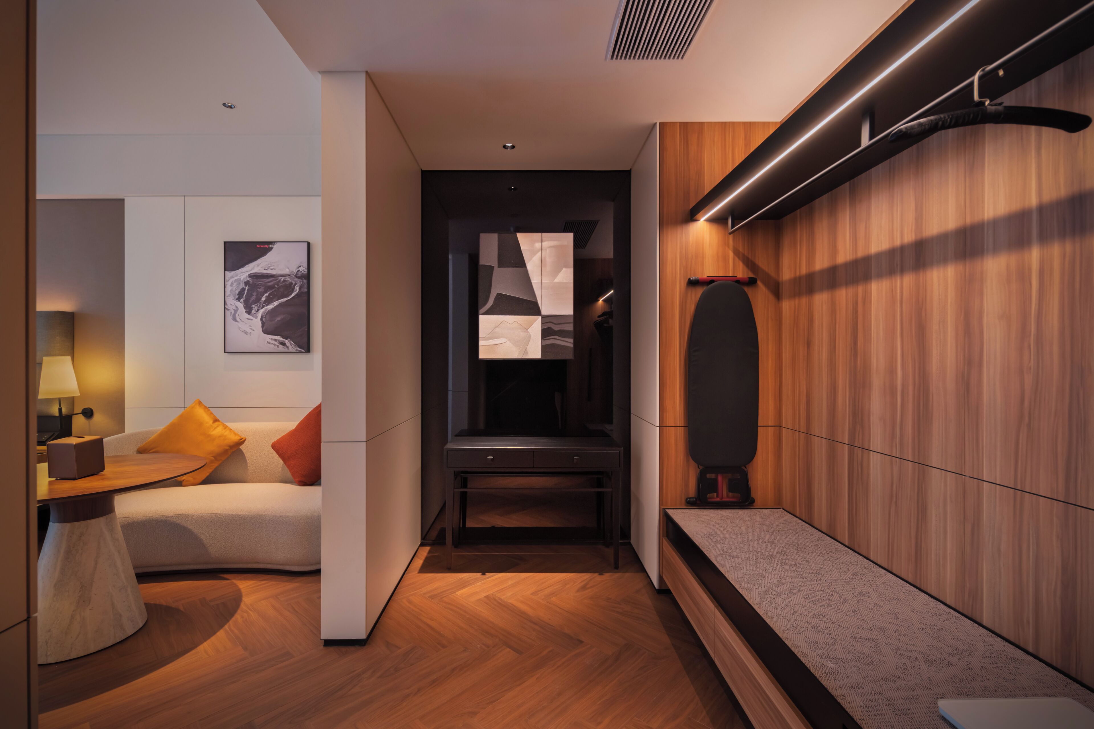 Moderni hotellihuone, jossa on sohva, pieni pöytä, penkki ja seinälle asennettu televisio.