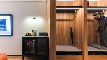 A modern hotel room with a wooden wardrobe, a small desk with a lamp, and a bed with a pillow.
