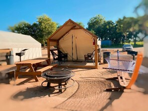Ein Campingplatz mit Zelt, Picknicktisch, Feuerstelle, Stühlen und einer Hängematte.