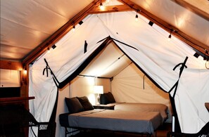Ein Zeltraum mit Bett, Lampe und Stuhl.