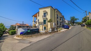 Una calle residencial con un edificio de dos pisos, coches estacionados y cielo despejado.