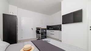 Un dormitorio moderno con cama, un sombrero, televisor, área de cocina y una puerta blanca.