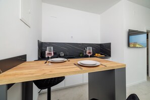 A modern kitchen with a wooden table set for two, a black marble backsplash, and a flat-screen TV mounted on the wall. - Modern studio with sea view & balcony in Crikvenica (Crikvenica)