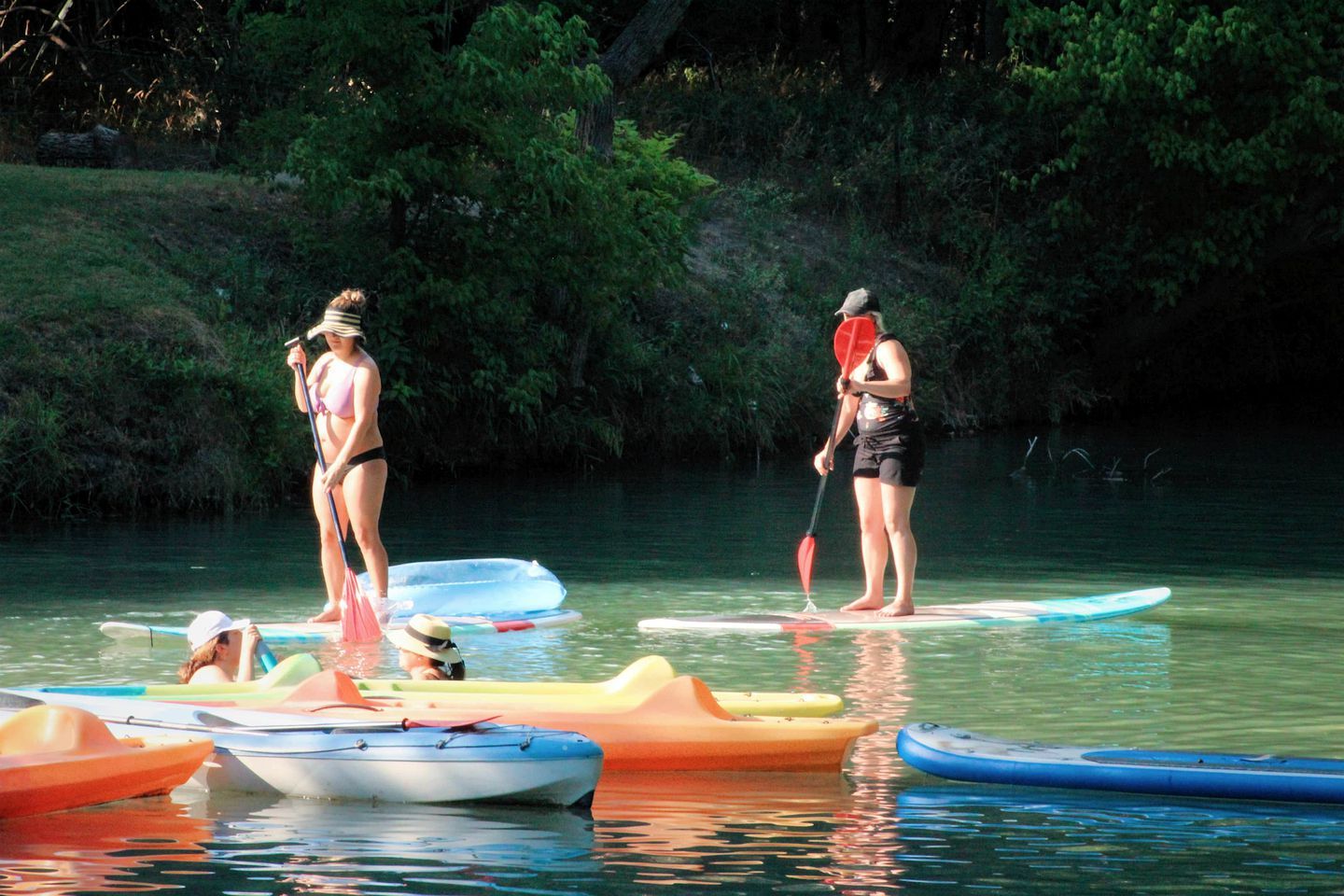 People on paddleboards in a calm body of water with various small boats around.