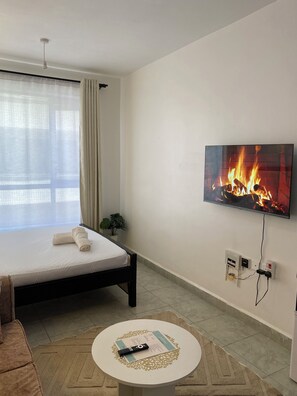 Ein Hotelzimmer mit Bett, Wandfernseher, kleinem Tisch mit Fernbedienung und Vorhängen am Fenster.