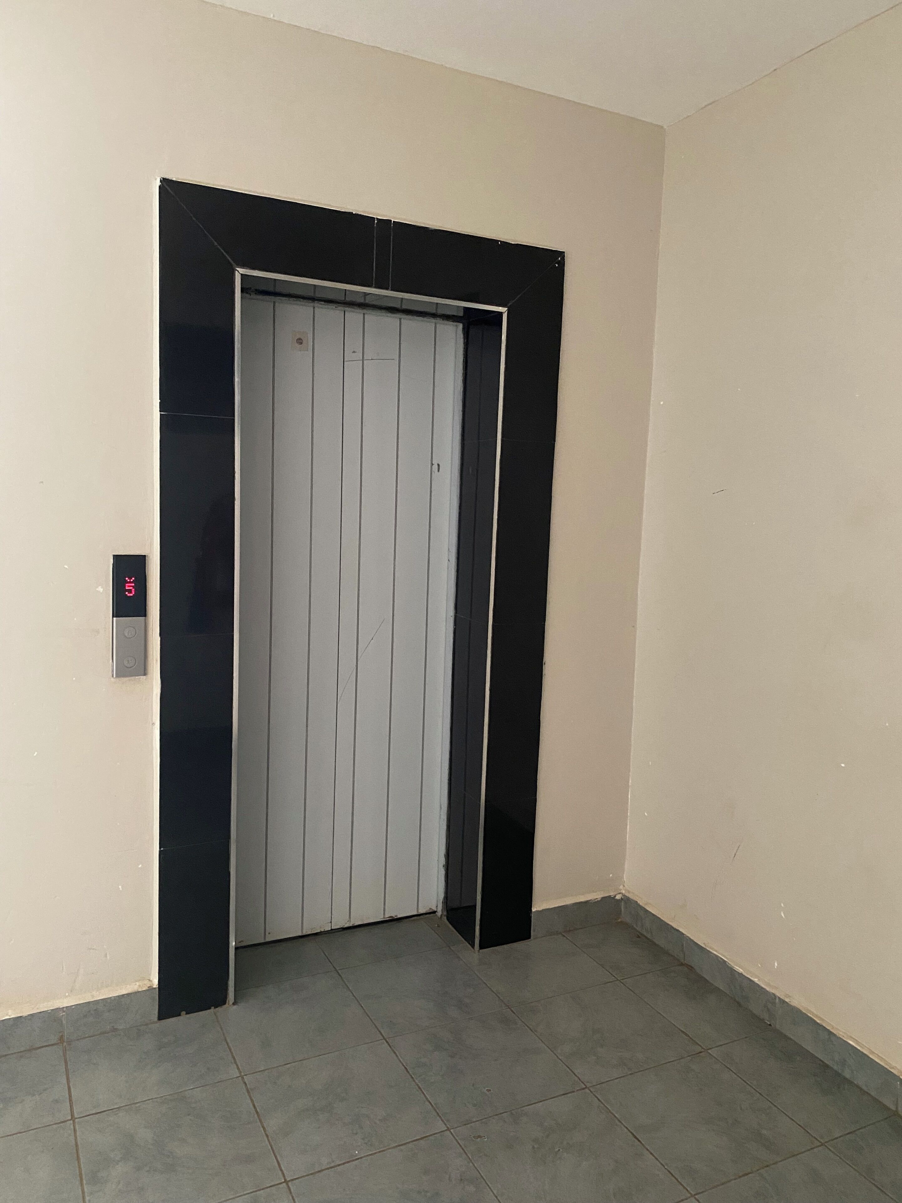 A closed elevator door in a hallway with a digital display and a button on the wall.