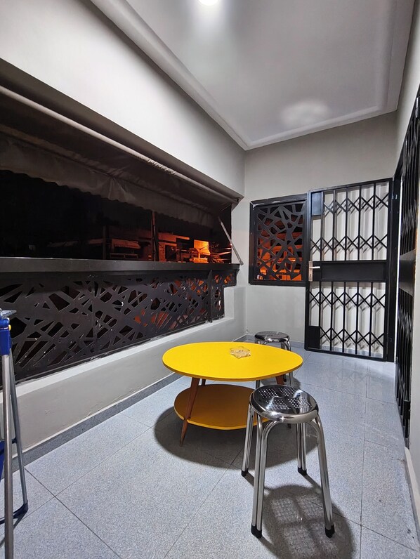 Une pièce avec une table jaune, deux chaises, une fenêtre ornée d’un paravent décoratif et un portail en métal.