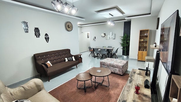 Een moderne woonkamer met een bank, salontafel, poef, eettafel, stoelen en een televisie.