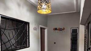 Een hal met een plafondlamp met een patroon, een raam met een metalen traliewerk, een welkomstmat en een potplant.