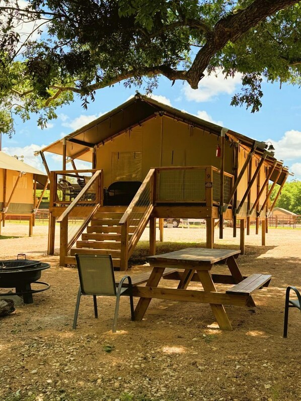 A rustic wooden structure with a staircase leading to a covered porch, a picnic table, and a grill.