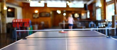 A ping pong table with a paddle and ball in a room with wooden ceilings and tables.