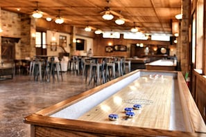 A bar area with a shuffleboard table, wooden ceiling, and bar stools.
