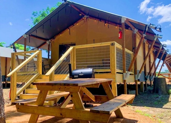 A wooden structure with a covered patio area, a grill, and a fenced entrance.