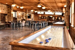 A bar area with a shuffleboard table, wooden ceiling, and bar stools.