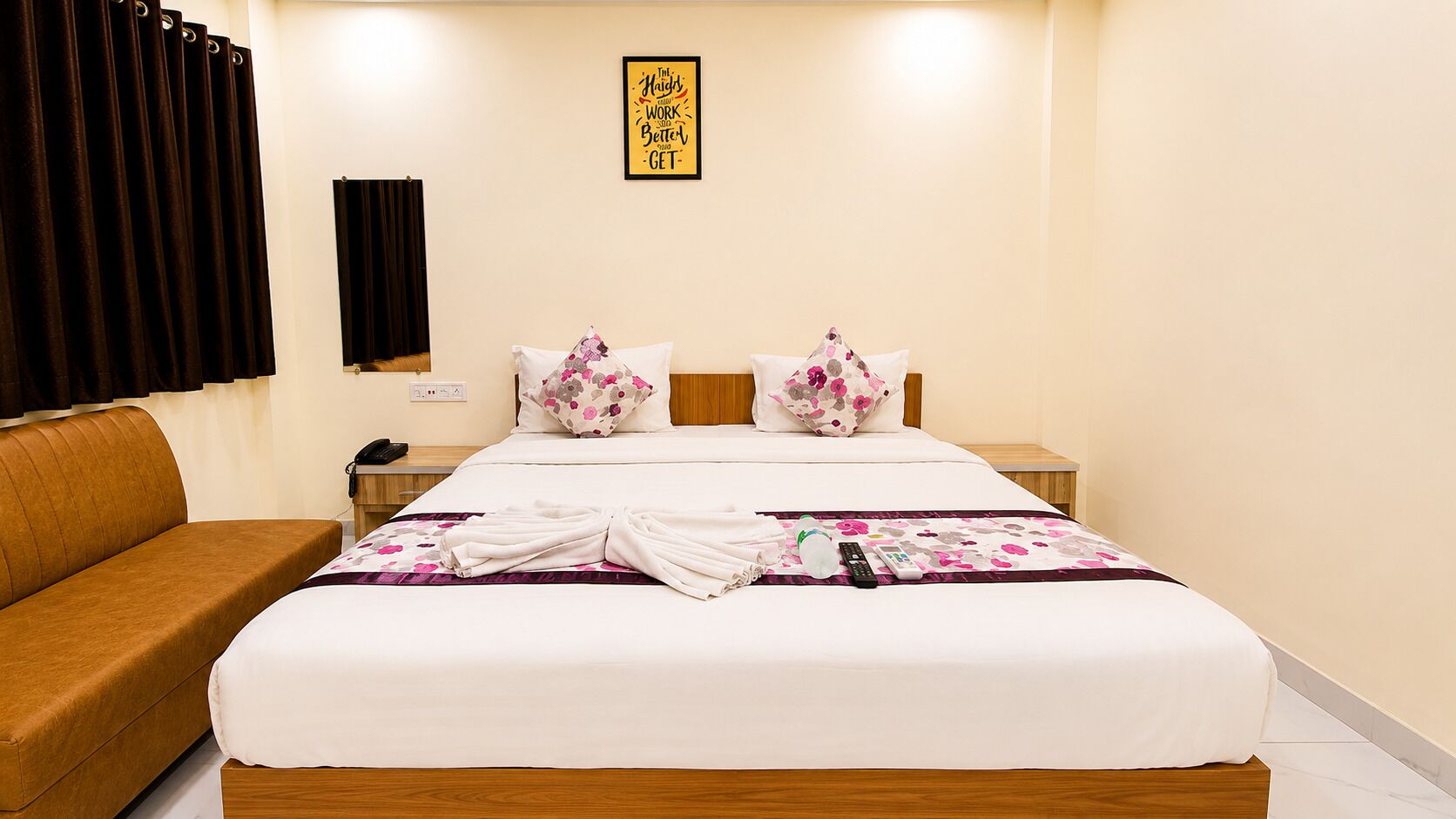 Habitación de hotel con cama, dos almohadas, mesita de noche con teléfono, sofá marrón y pared con una cita enmarcada.