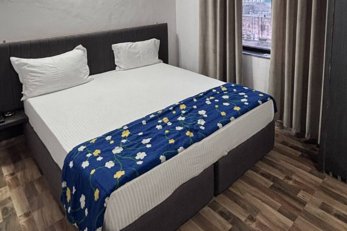 A bedroom with a bed, a ceiling fan, a window with curtains, and a view of the city.